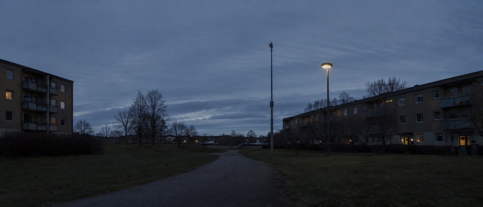 Svenskt bostadsområde i skymningsljus med gångväg och tänd gatlykta